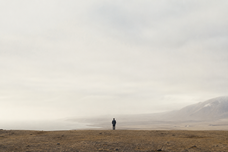 A person standing alone on a bluff above a misty coastline